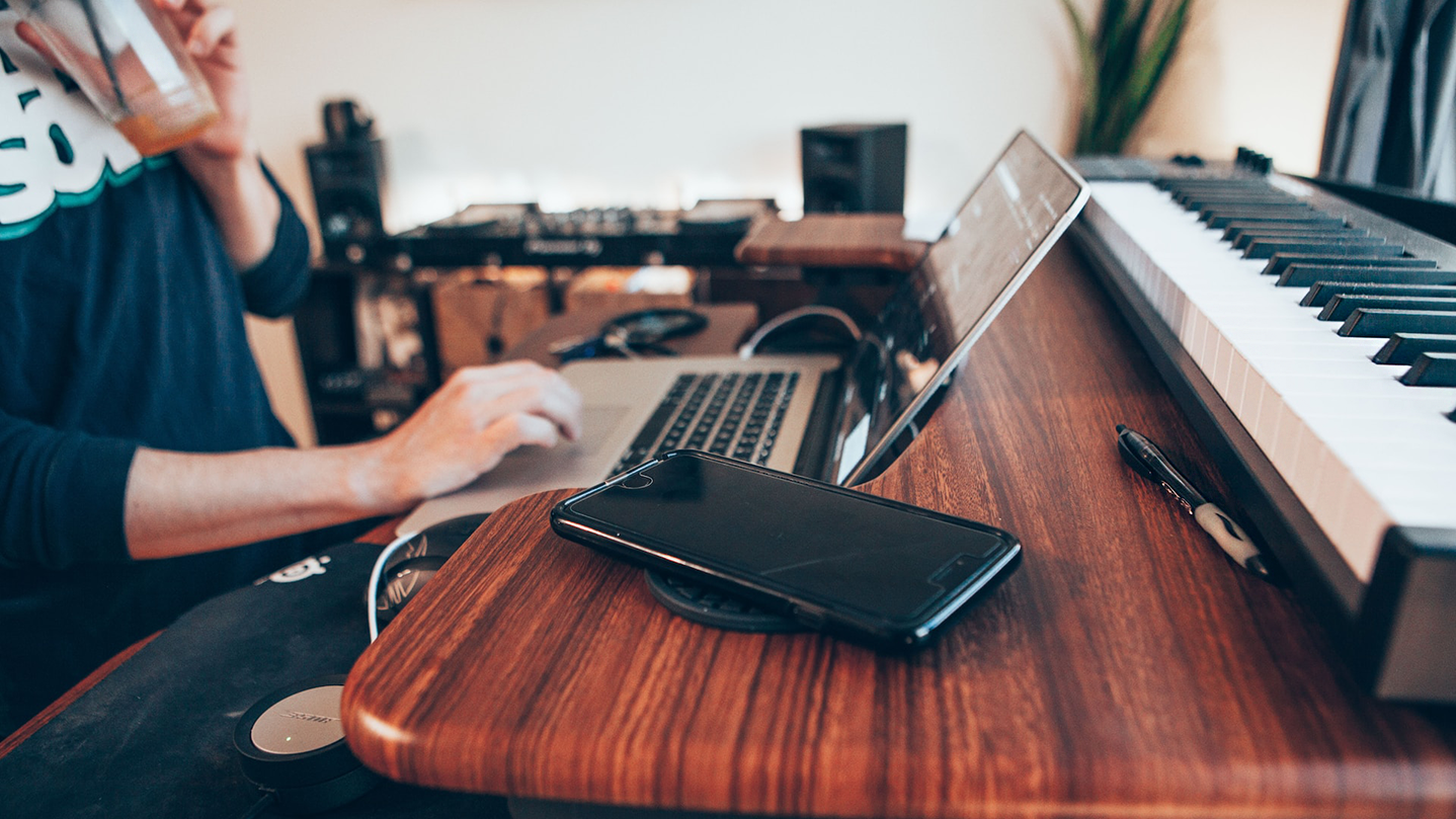 Person seated at their laptop, with a piano keyboard and phone on the desk.
