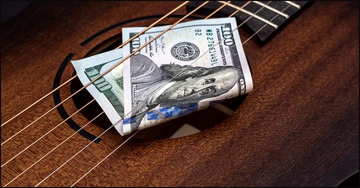 one hundred dollar bill in the strings of an acoustic guitar