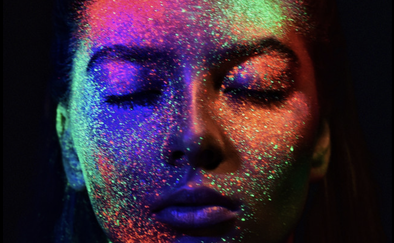 Neon face paint glowing under UV light, vibrant colorful artistic makeup on a woman's face, creative makeup art for night events and festivals, close-up photo for beauty and fashion editorial.