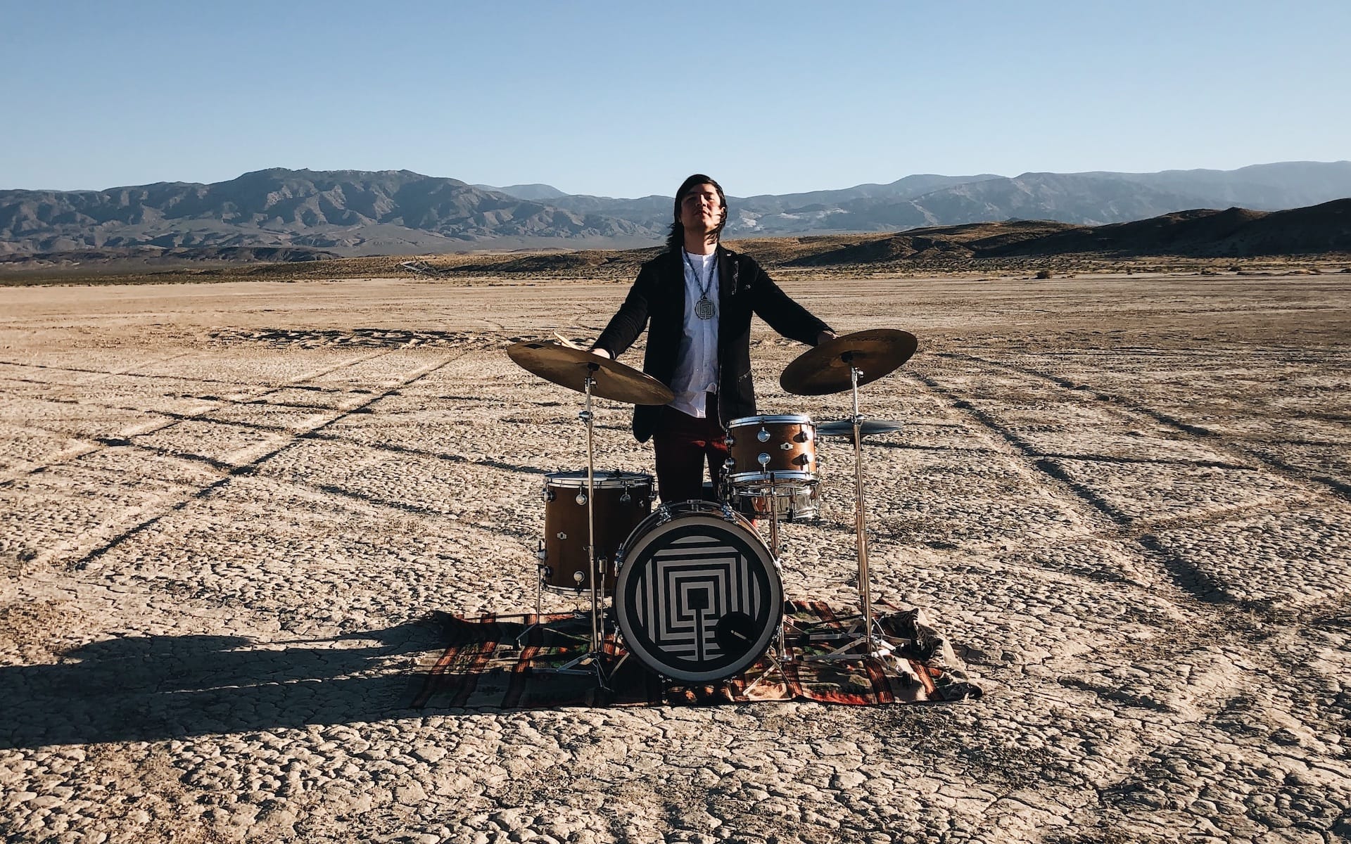 Across the desert landscape, a musician performs on a drum set, symbolizing innovation and creativity in the music industry. The expansive, arid environment contrasts with the vibrant energy of modern music production.