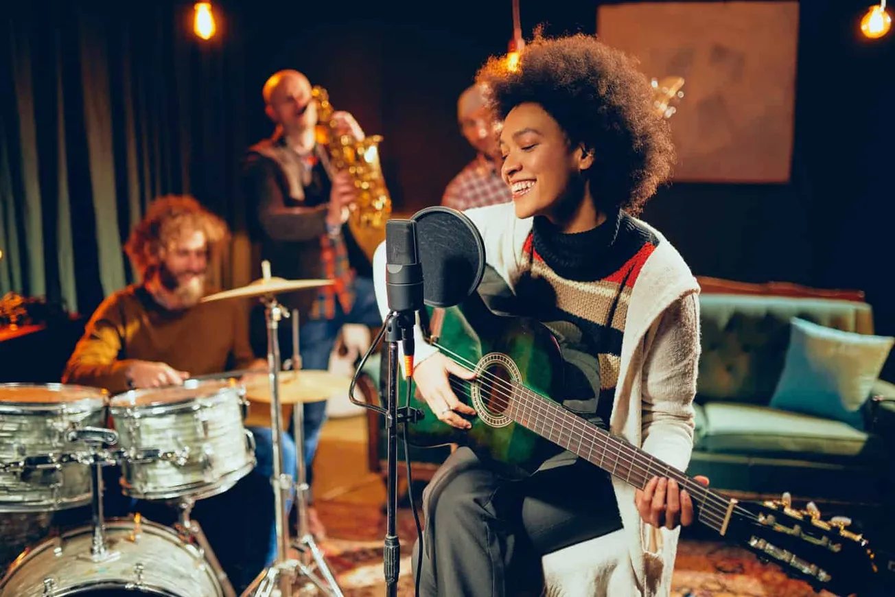Young woman performing guitar and singing with a band of jazz musicians in a cozy studio.