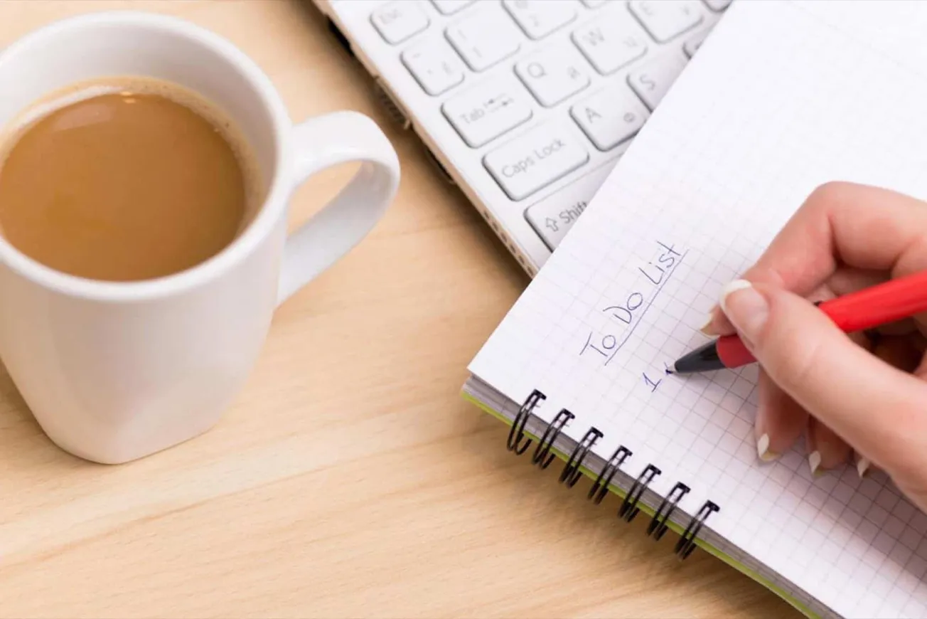 A cup of coffee, a keyboard, and a handwritten to-do list on a notebook, representing productivity, planning, and organizatio