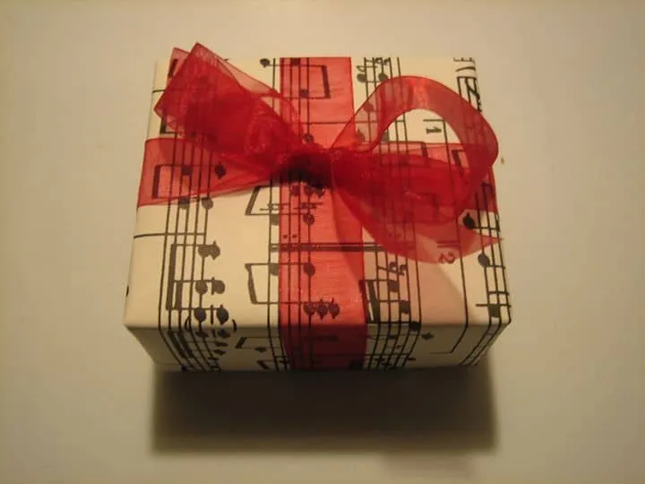 Gift box wrapped with musical notes and red ribbon, musical-themed present for music lover, artistic gift wrapping related to