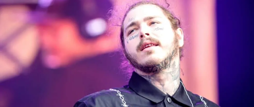 Someone performing on stage at a music event, showcasing a tattooed artist with a confident expression, colorful lighting, li