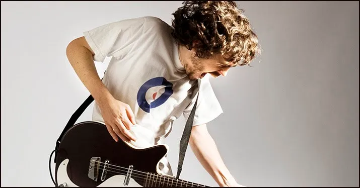 Guitarist playing guitar passionately, wearing a white t-shirt with a logo, engaging in music performance or practice.