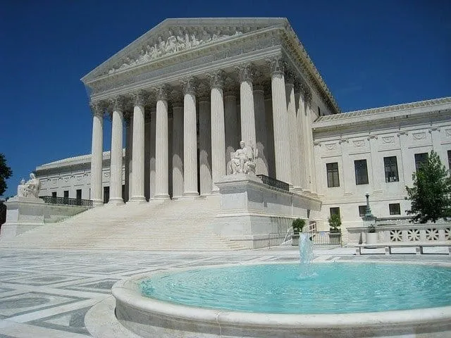 Imposing Greek-style government building with tall columns and marble facade, surrounded by a pond with a fountain, represent