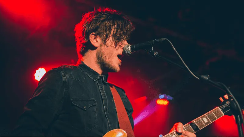 Soft-focus photo of a young male musician playing an electric guitar and singing into a microphone on stage with vibrant red