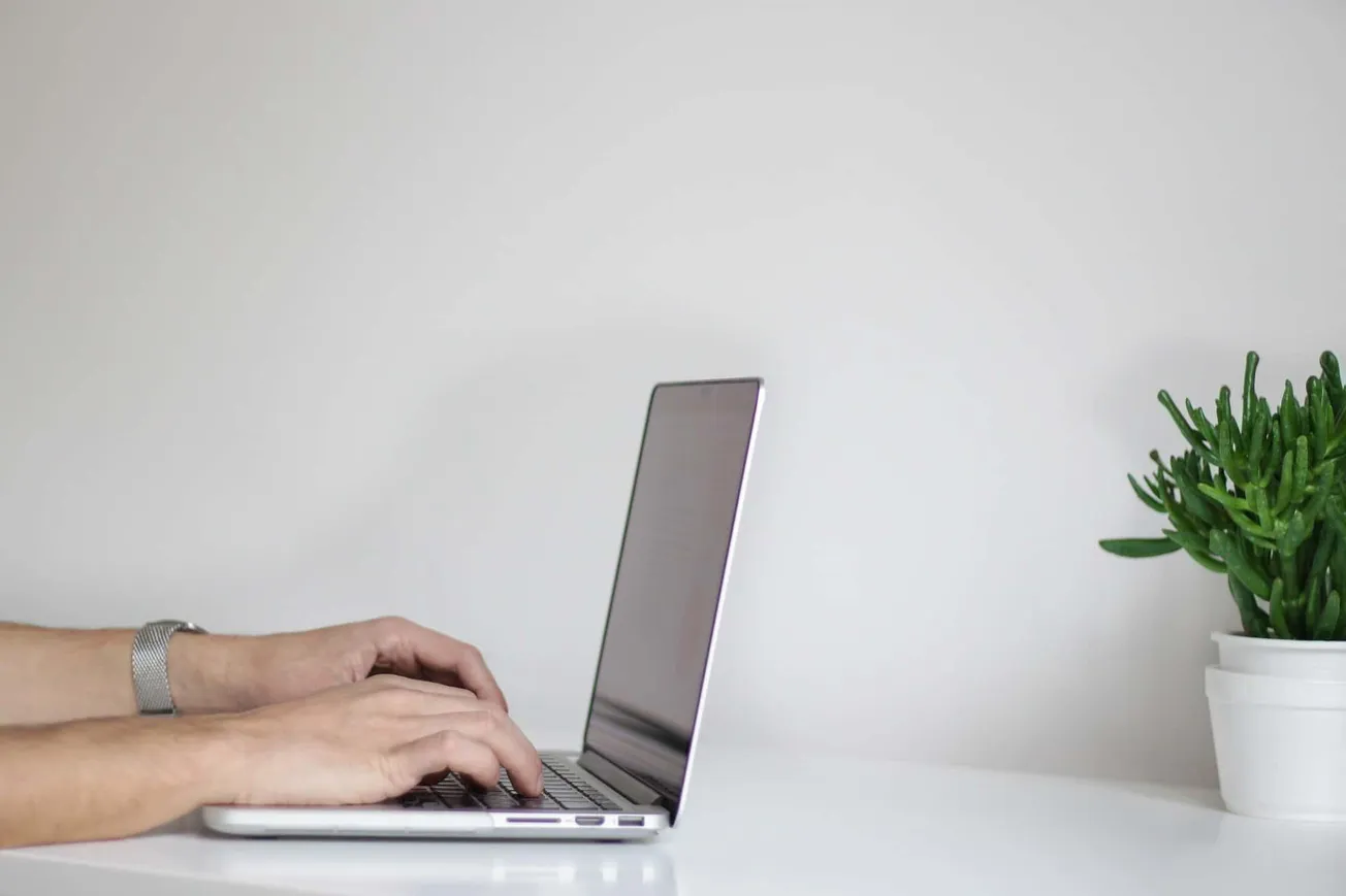 Laptop computer on a white desk with a small green plant, minimalistic workspace, modern office setup, technology, remote wor