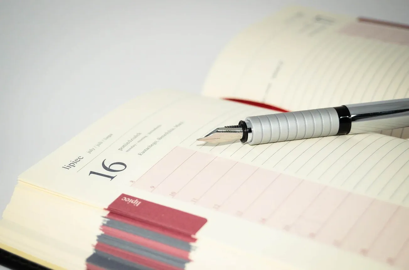 A silver fountain pen resting on an open planner with dated pages, highlighting organization and scheduling tools.