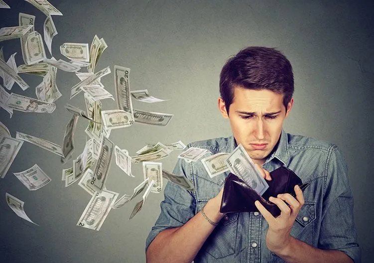Stack of dollar bills flying out of a wallet with a worried young man looking at his phone, representing financial stress or