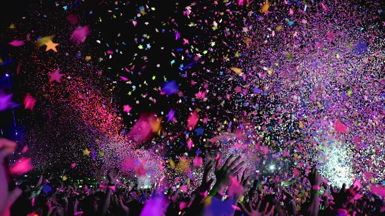 Bright concert crowd with colorful confetti and vibrant lights at a music event or festival.