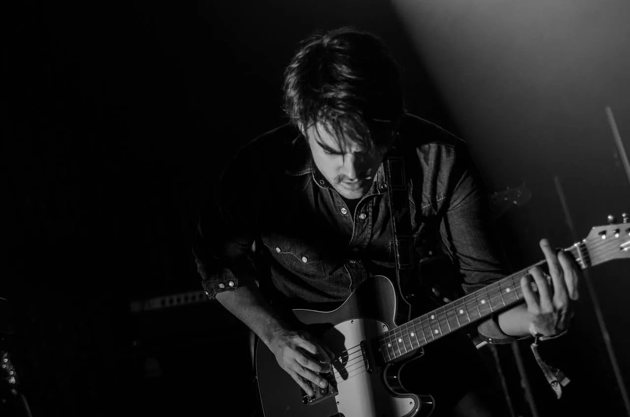 Guitarist playing electric guitar during live music performance in dark setting, black and white image.