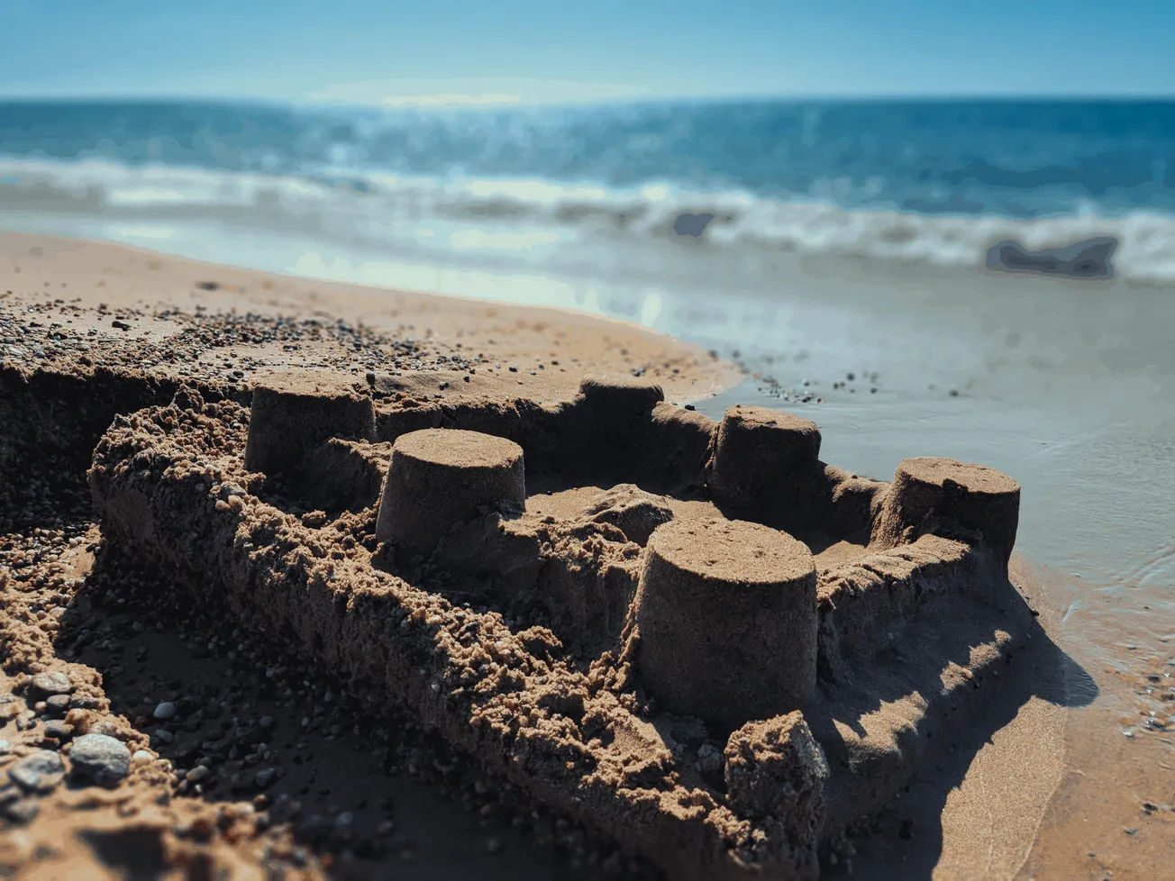 Sandcastle on the beach with ocean waves in the background, showcasing a summer beach scene ideal for travel, leisure, and va