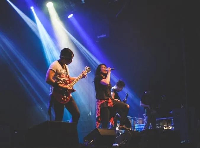 Guitarist and singer performing live on stage at a music concert with vibrant stage lighting.
