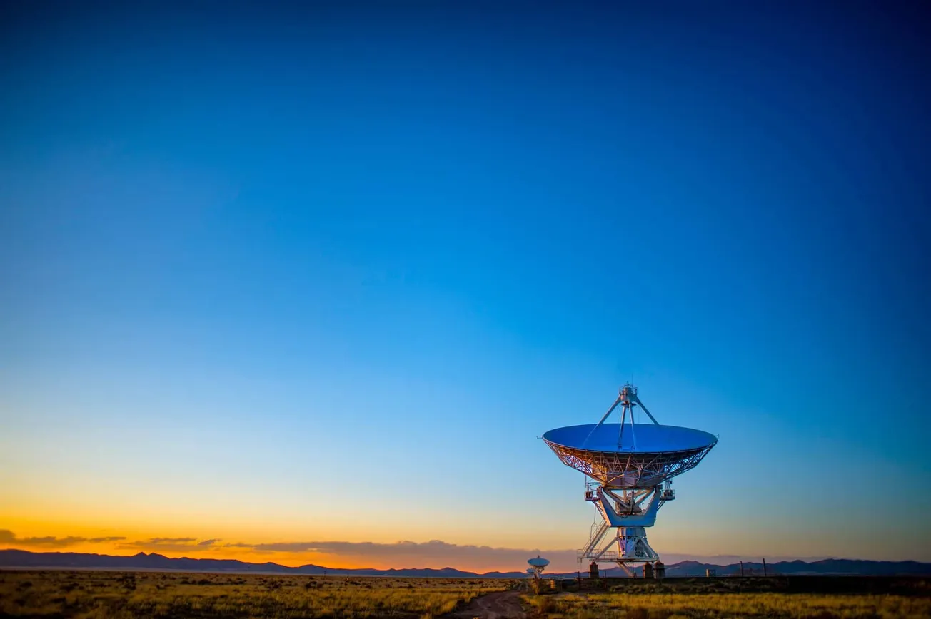 Large radio telescope antenna observing the sunset in the desert, with mountains in the background, representing advances in