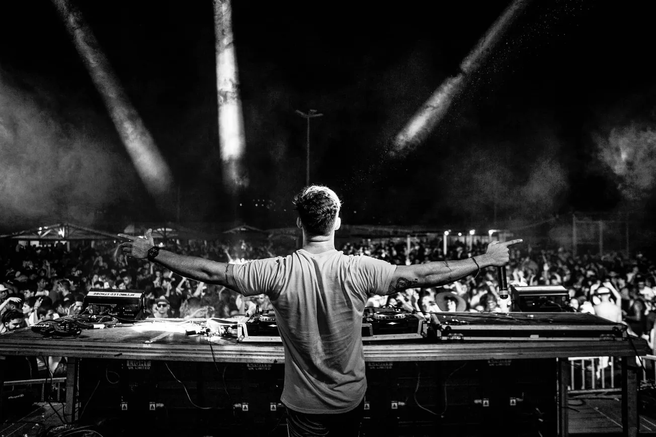 Energetic DJ performing at a night concert with a large crowd, stage lights, and music equipment.