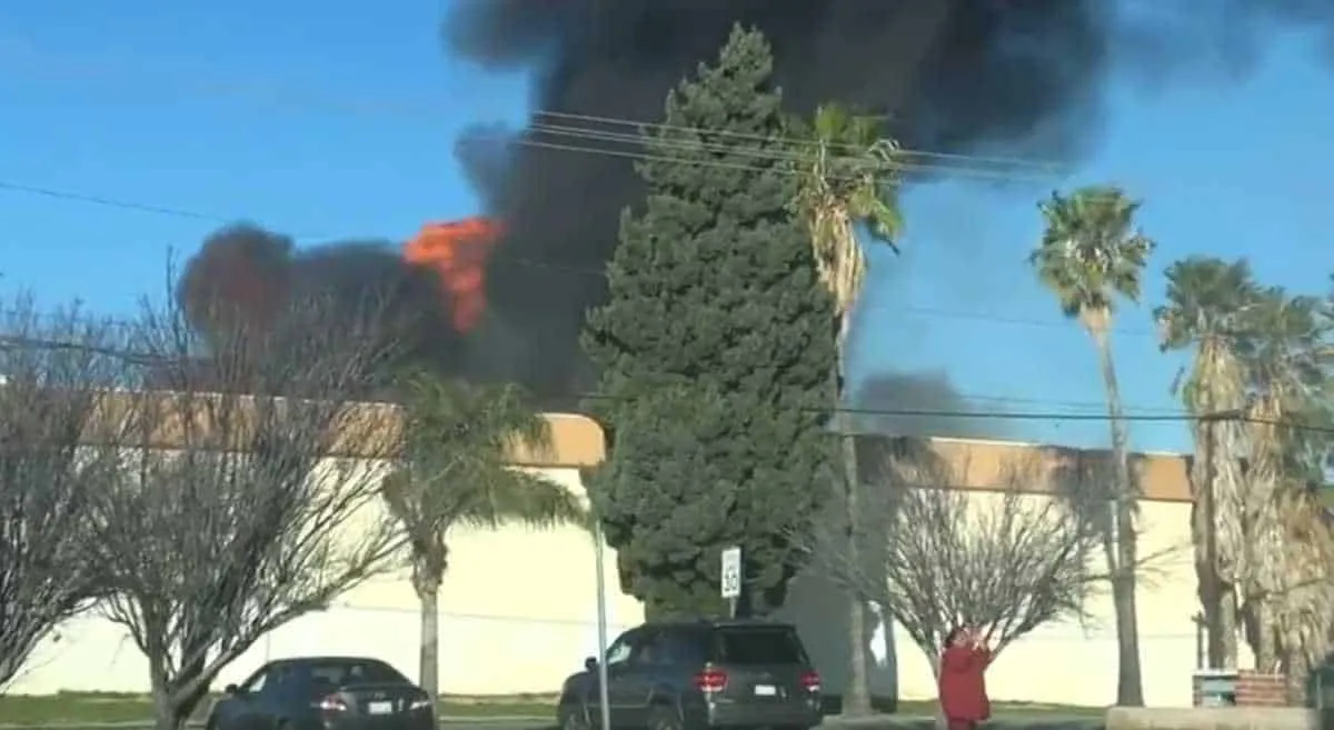 Fire emergency wildfire burning in urban area with thick black smoke and flames behind trees and building, emergency response