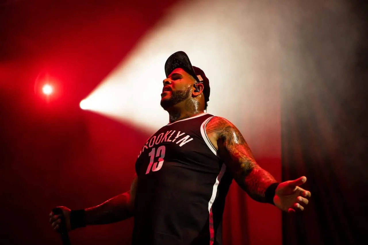 Vibrant live concert image featuring a tattooed rapper in a Brooklyn jersey performing under dramatic red and white stage lig
