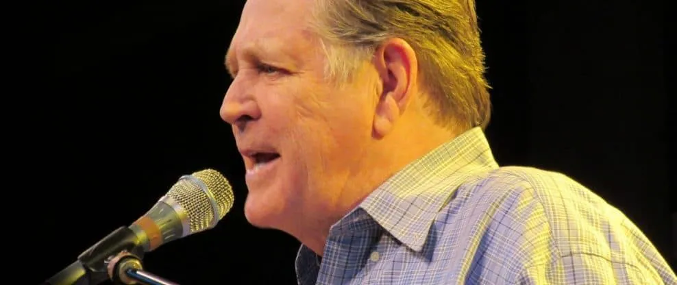 Renowned male speaker passionately delivers a speech at a microphone during a public event or conference.