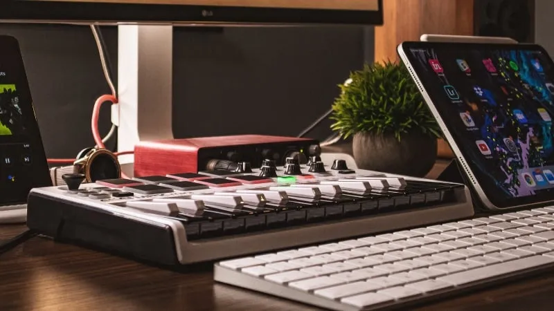 Portable music production setup with MIDI controller, tablet, and keyboard on a wooden desk for digital music creation and DJ