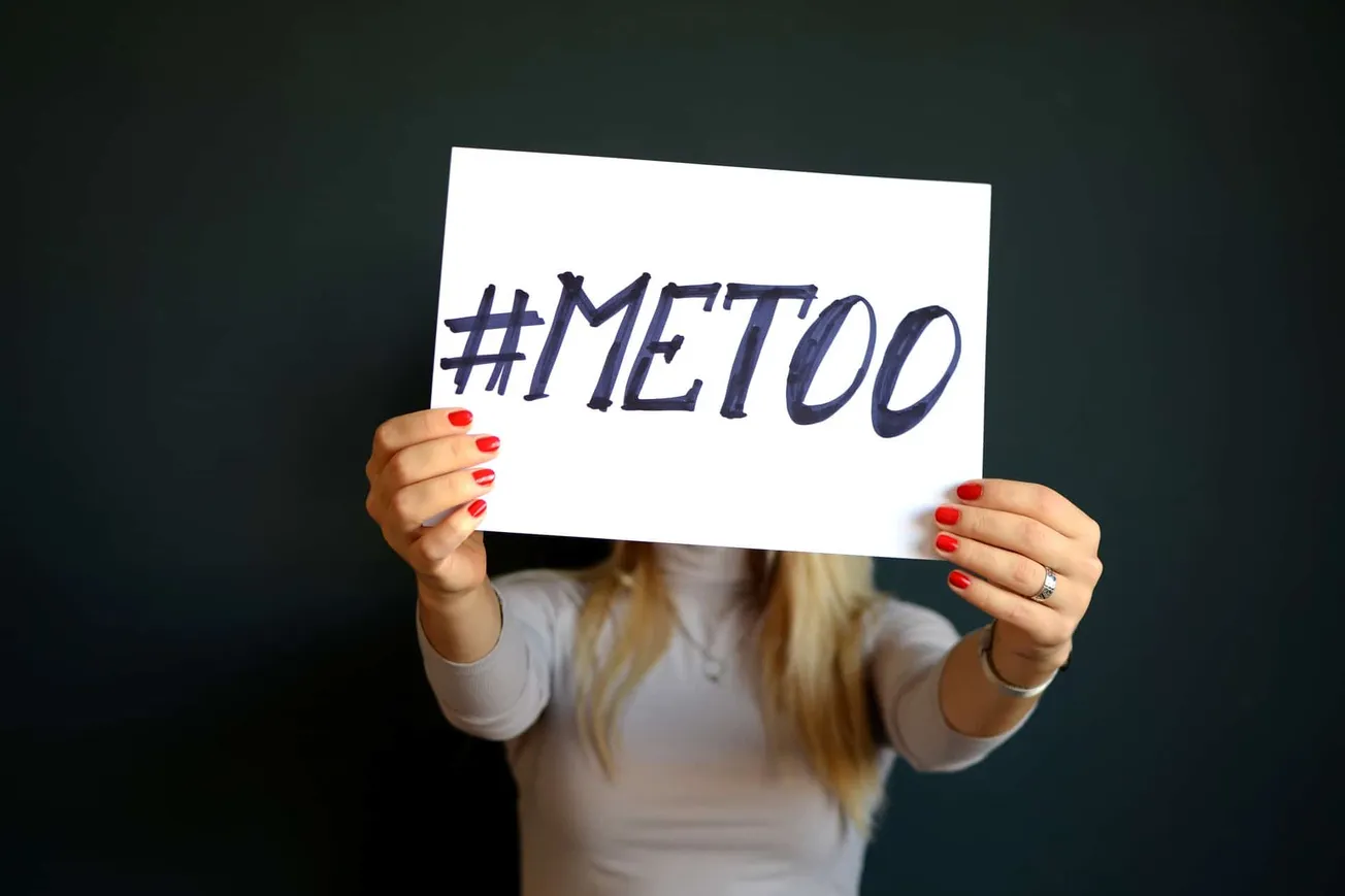 Hashtag #METOO on a white sign held by a person with red nail polish and a ring, symbolizing the social movement advocating f