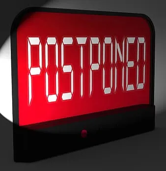 Postponed digital alarm clock with red LED display showing the word "POSTPONED" in bold letters, highlighting delays or resch
