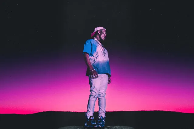 Man standing on rocky terrain during vibrant sunset with pink and purple sky, showcasing music, creativity, and artistic expr