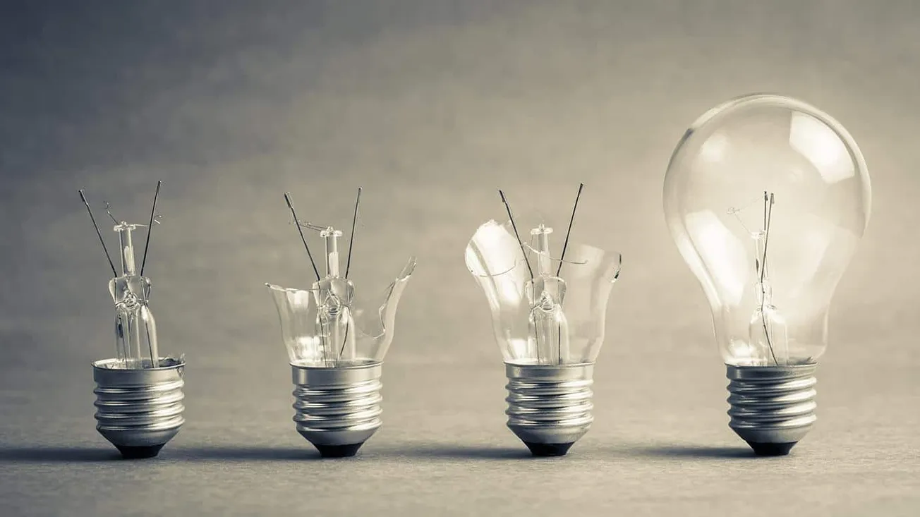 Broken lightbulbs representing ideas and innovation, transitioning to a glowing, fully intact bulb symbolizing creativity and