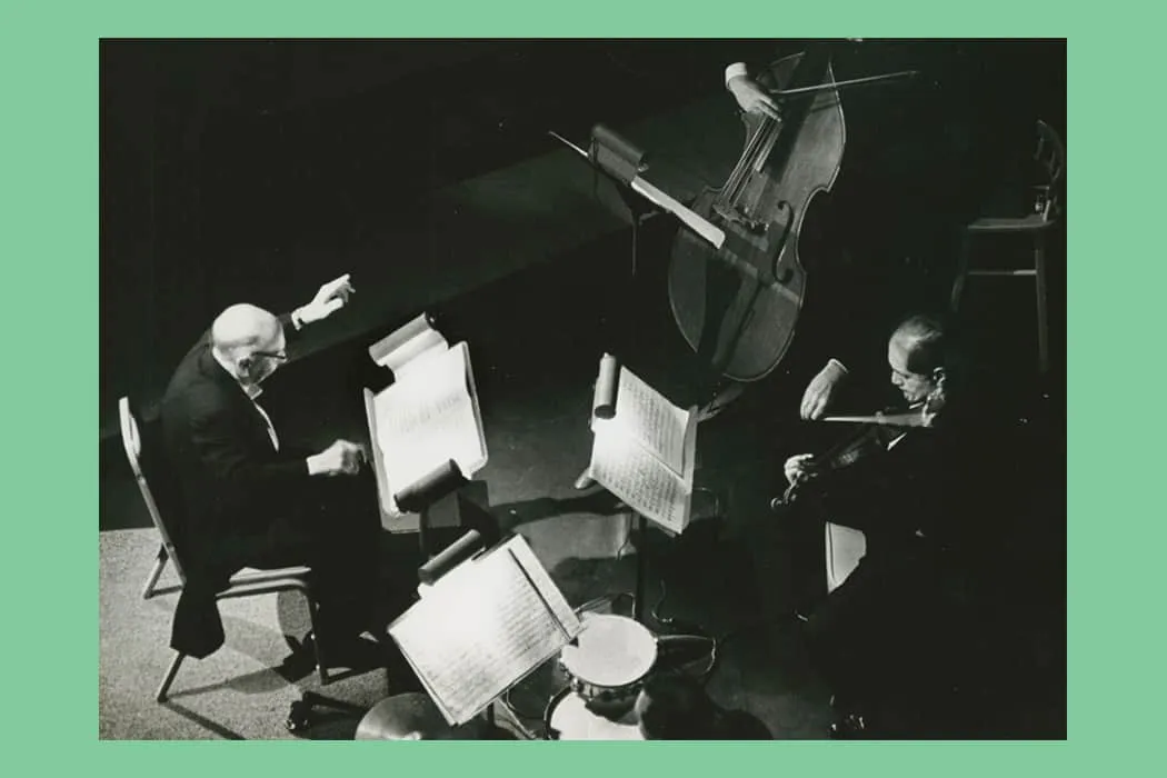 Elderly classical musicians performing a duet with a piano and violin on stage during a concert.