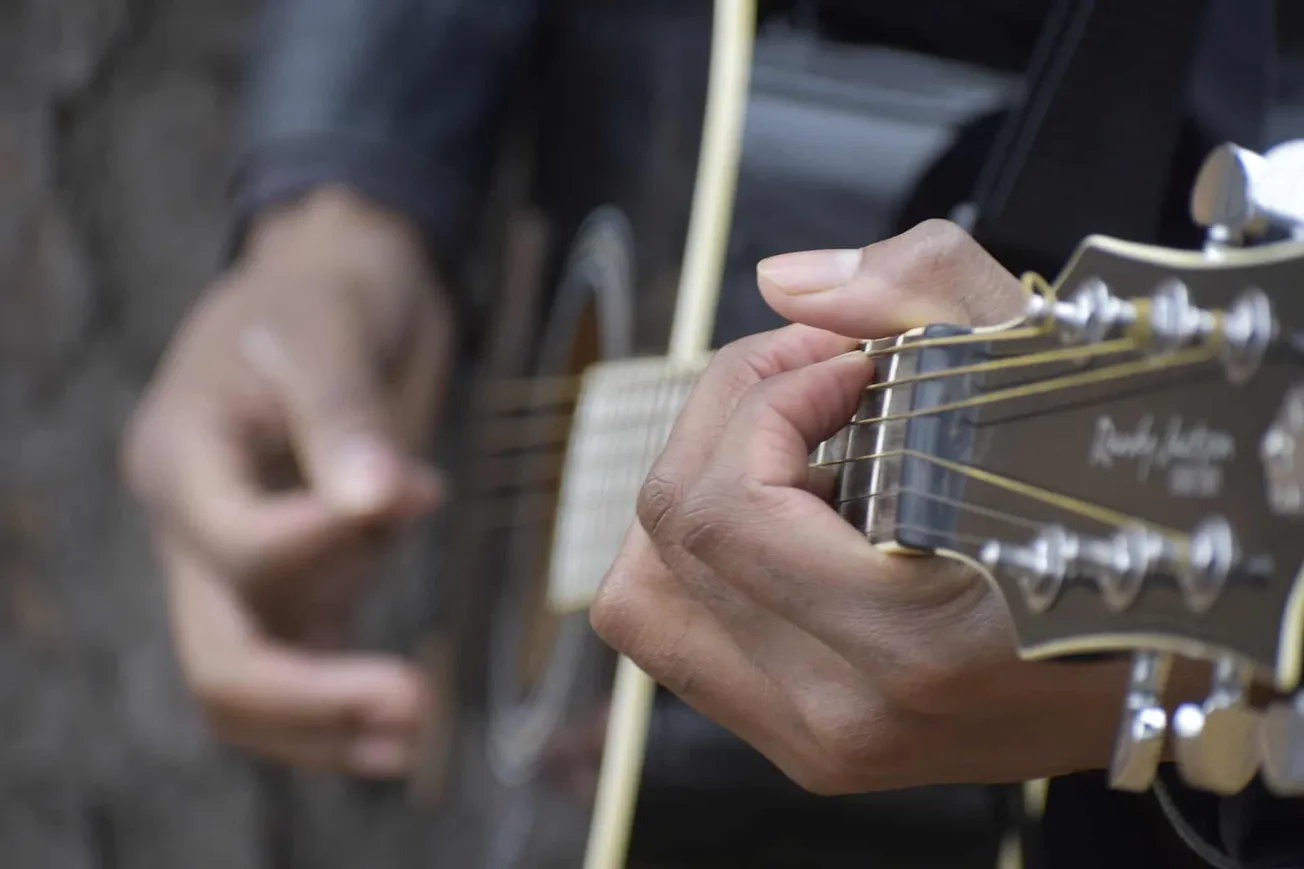 Acoustic guitar player hand close-up, focusing on fingers pressing strings on fretboard, live music performance, musician pla
