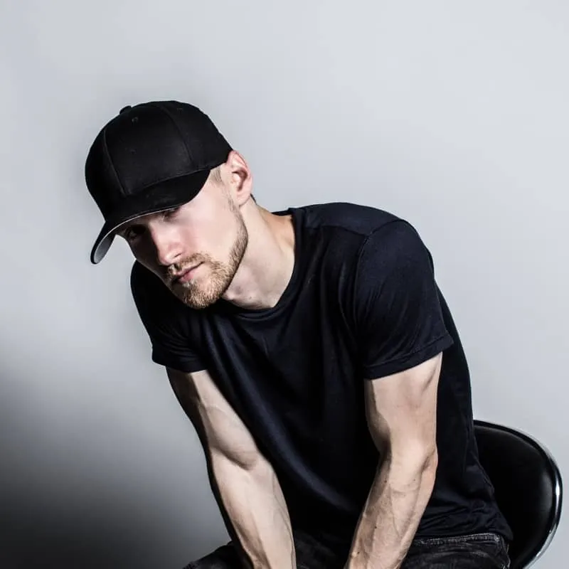 Young man wearing black baseball cap and t-shirt, studio portrait, casual style, modern fashion, neutral background.