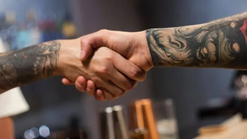Handshake between two tattooed individuals symbolizing partnership or agreement, captured in a professional and modern settin