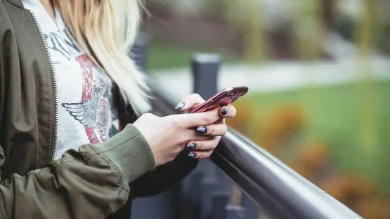 Girl using smartphone outdoors on park bench, casual fashion, reading or texting, autumn setting, social media, digital commu