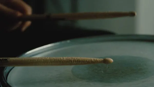A close-up of drumsticks hitting a drumhead, emphasizing music performance and musician skill.