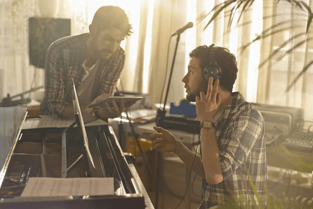 Professional musicians recording in a home studio, working on music production with headphones, a piano, and audio equipment,