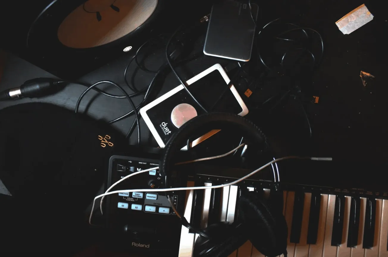 DJ setup with turntable, keyboard, headphones, and electronic devices on a dark music studio desk for music production and li