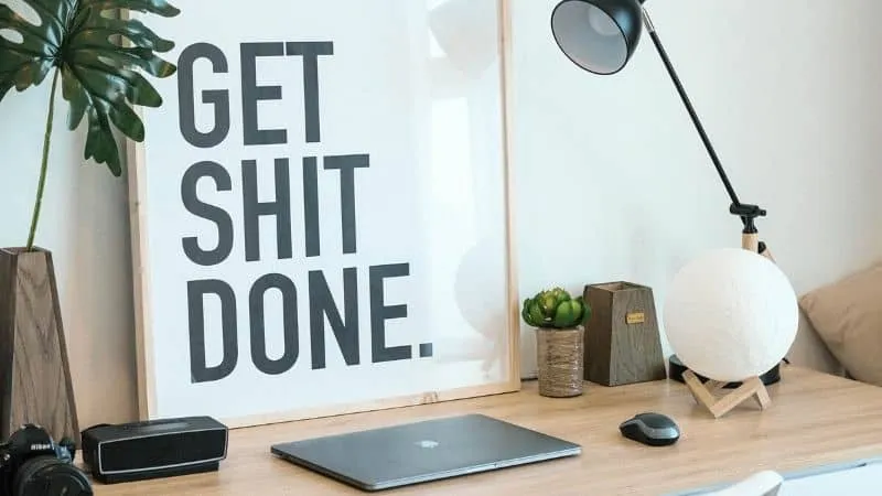 Get shit done motivational quote displayed in modern workspace with tech accessories and decorative items.
