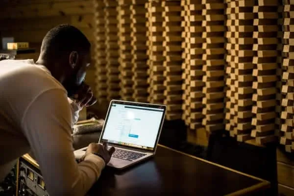 Laptop user working in a soundproof studio with acoustic foam panels for music or audio production.