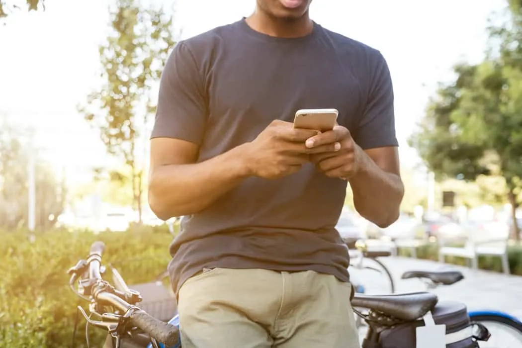 Young man using smartphone outdoors with bicycles in park, digital music, social media, technology, urban lifestyle, Hypebot,