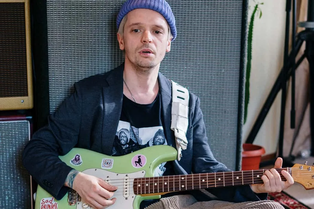 Viral musician playing an electric guitar in a music studio, face focused on performing, surrounded by amplifier speakers and