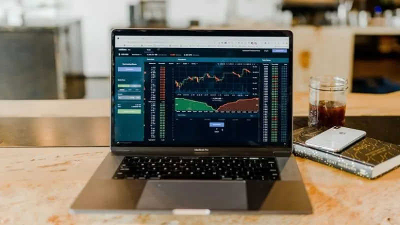 Laptop displaying cryptocurrency trading charts on Hypebot website, with stock market data and analytics.