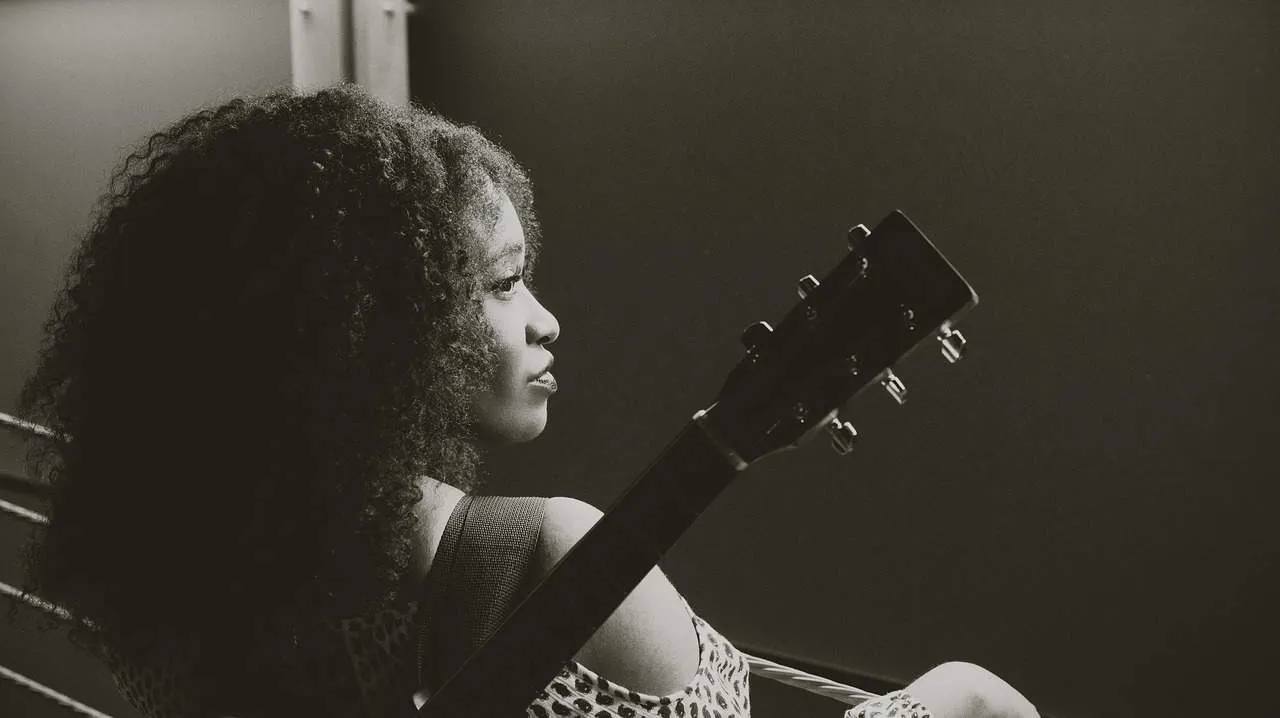 Thoughtful African American woman with curly hair sitting by a window, gazing outside in black and white, capturing a moment