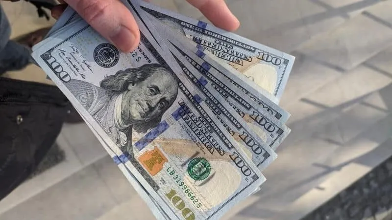 Hundred-dollar bills being held in a person's hand, showcasing cash, money, and financial exchange.