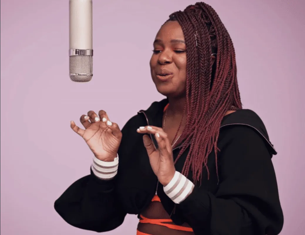 A woman singing into a microphone on a purple background, performing passionately in a music recording studio or podcast sett