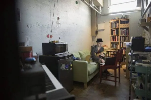 Cozy music studio with a person playing guitar in a well-lit, industrial-style room with bookshelves, sound equipment, and a