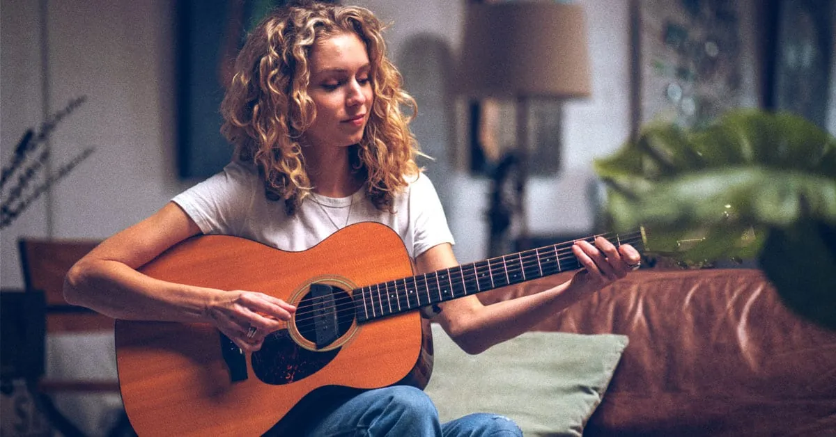Relaxed young woman playing acoustic guitar in cozy home setting, practicing music, showcasing musical talent, and creating a
