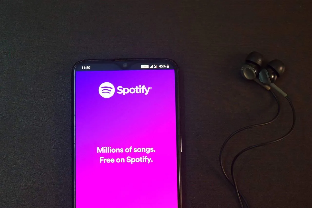 Spotify app on smartphone with wireless earphones, showcasing music streaming service.