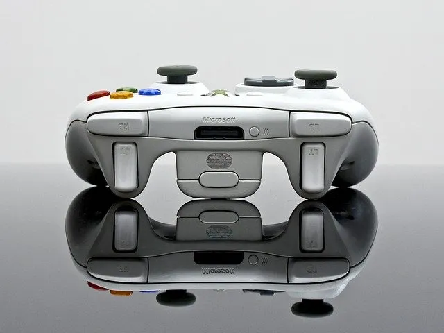 Gaming controller on reflective surface, close-up of white Microsoft Xbox controller with colorful buttons, used for gaming a