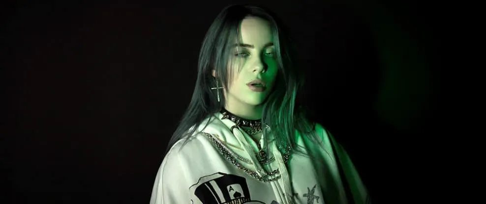 Bold young woman with dark hair wearing edgy fashion jewelry and a satin jacket, illuminated by dark green lighting against a