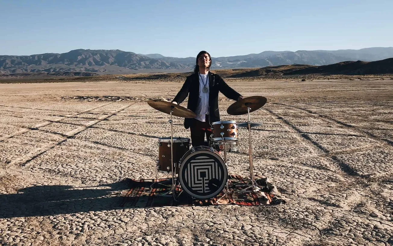 Across the desert landscape, a musician performs on a drum set, symbolizing innovation and creativity in the music industry.